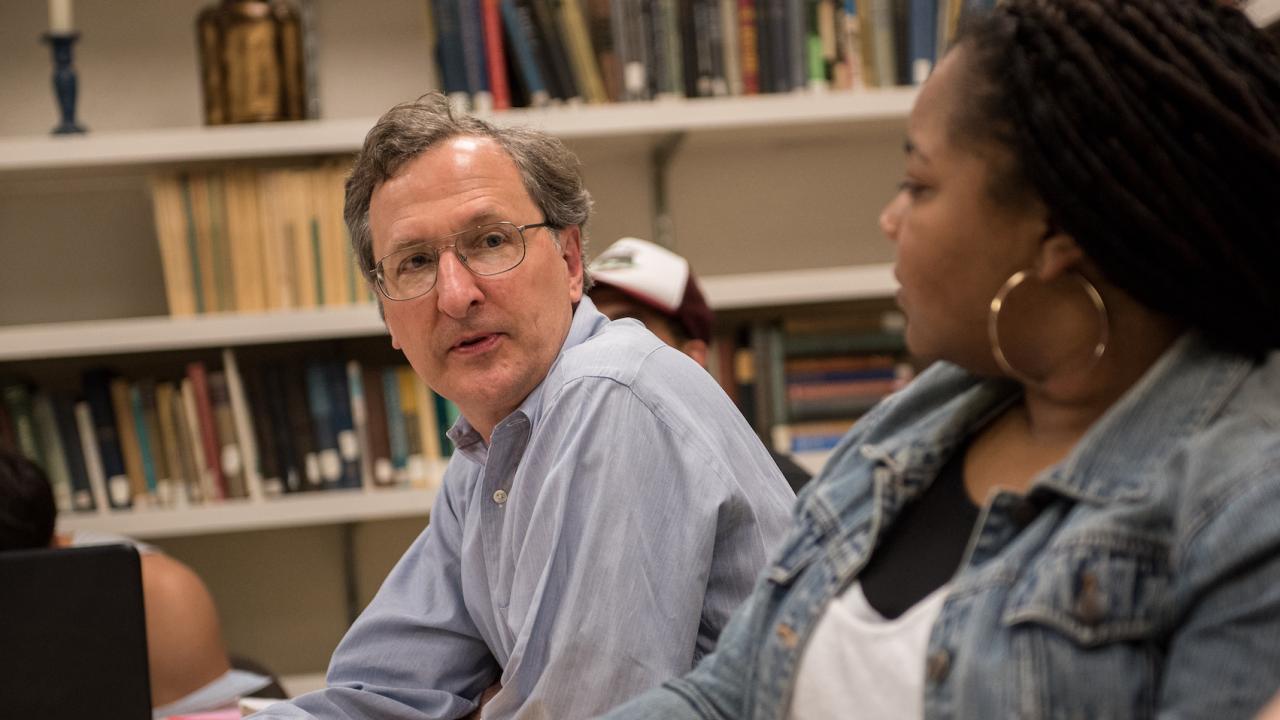 an with glasses turning toward a woman with long dark hair bookshelves in the background