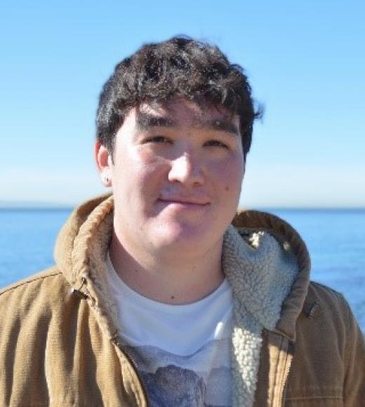 A man wearing a brown jacket with the ocean in the background