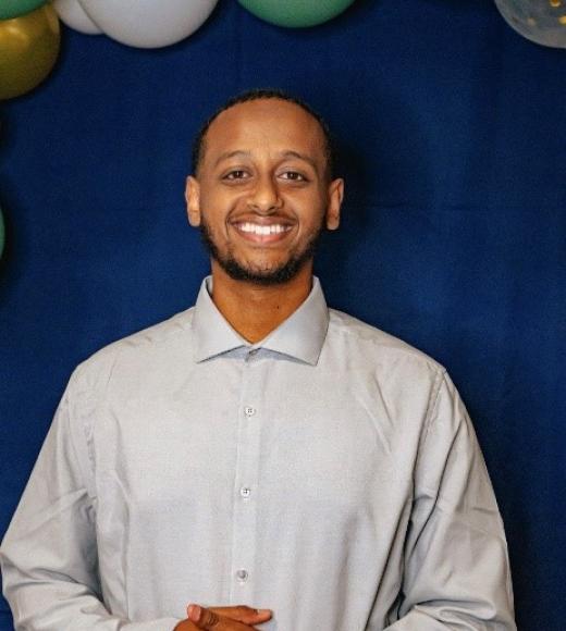 A man wearing a white collared shirt, under green and white balloons