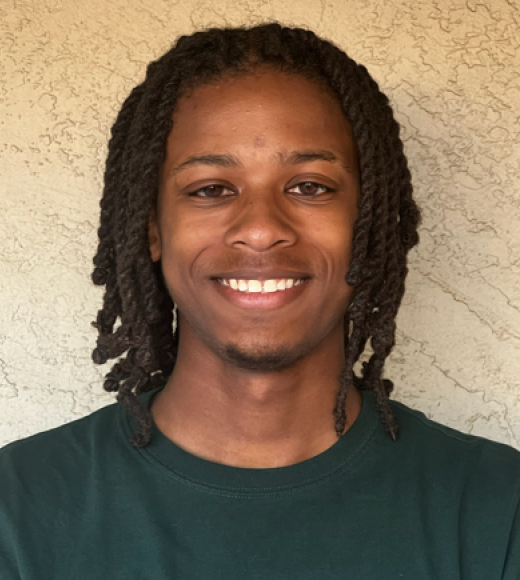 Smiling young man with shoulder-length twists, green shirt, beige textured wall