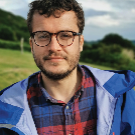 A man wearing a blue jacket, red and blue plaid, and glasses